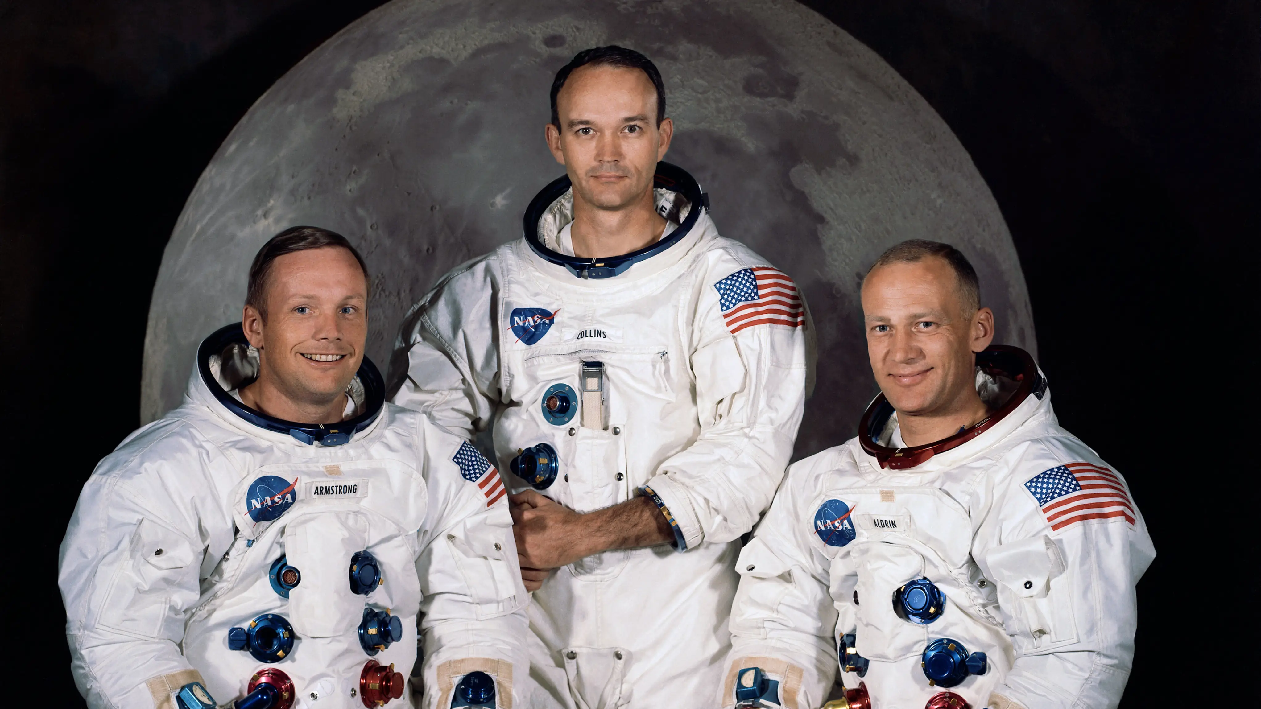 Iconic photo of three astronauts standing in front of a picture of the Moon.