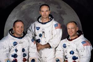 Iconic photo of three astronauts standing in front of a picture of the Moon.