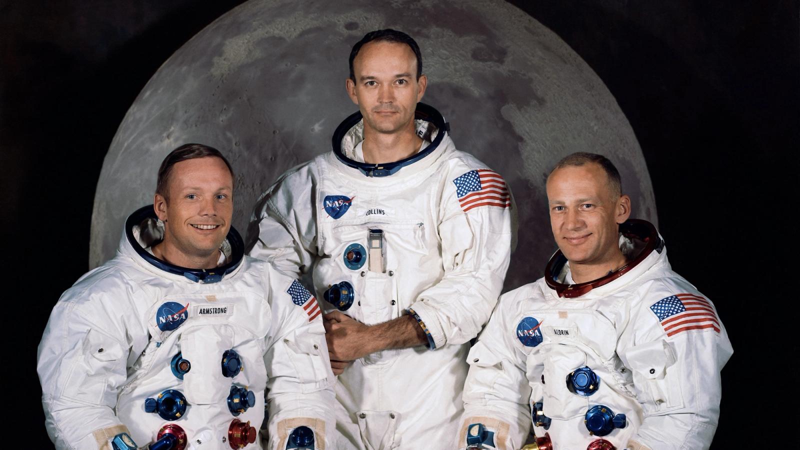 Iconic photo of three astronauts standing in front of a picture of the Moon.