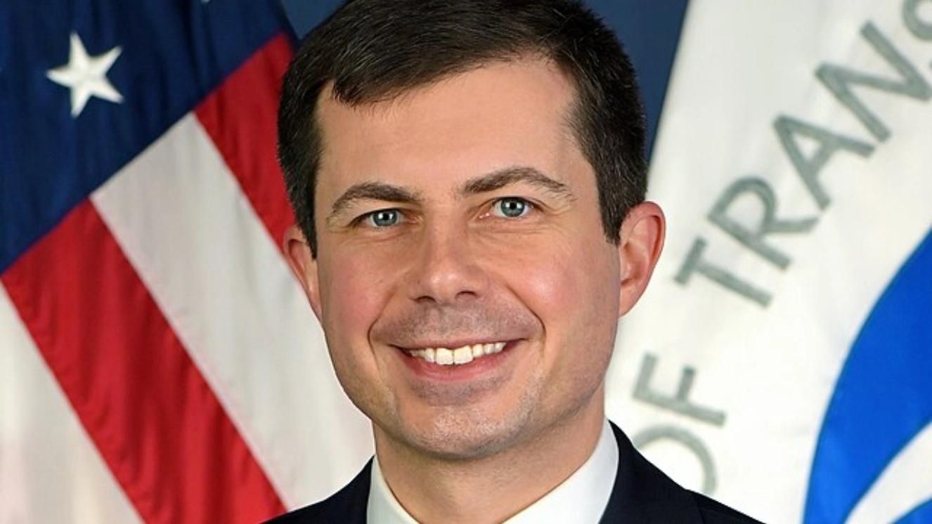 Pete Buttigieg smiling in front of U.S. flag and Department of Transportation emblem