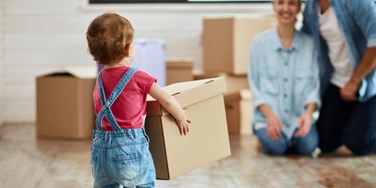 A toddler walks toward a parent with a moving box.