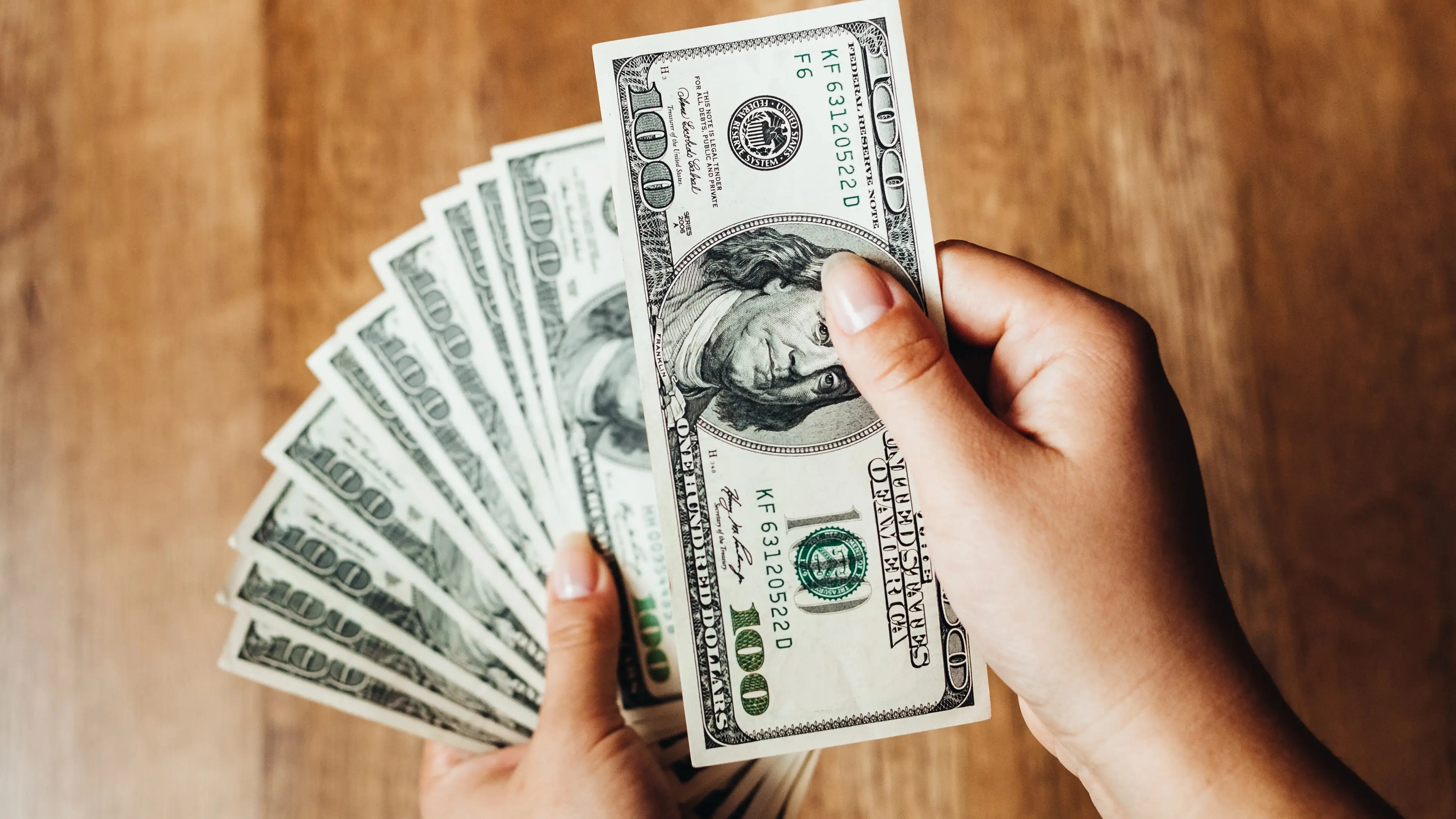 Closeup of hands counting 100-dollar bills.