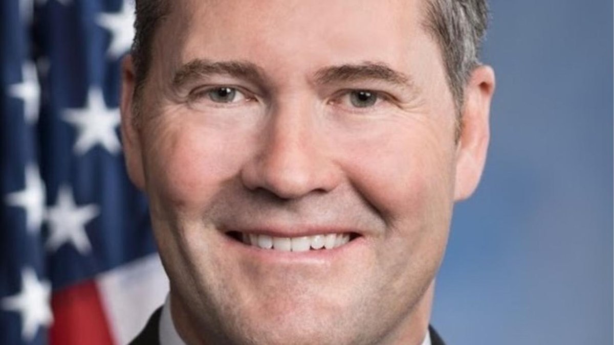 Rep. Mike Waltz smiling against a backdrop of the American flag.