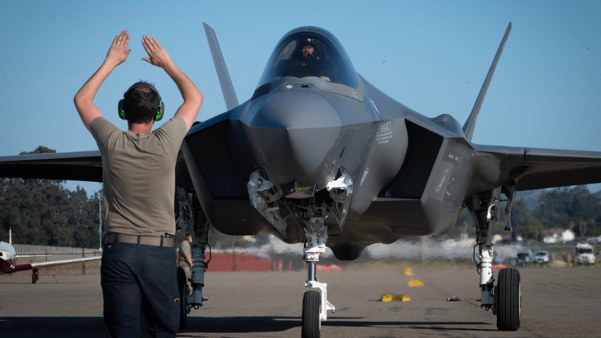 A soldier acts as a marshaller for a fighter jet.