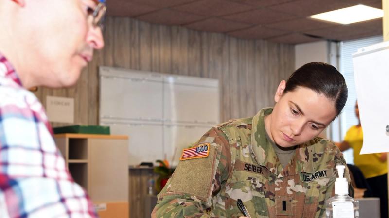 1st Lt. Sarah Seiber, chemical officer for 3rd Battalion, 337th Regiment Training Support Battalion, fills out paperwork while Gabe Barrera, transitions clerk for Tatitlek Corporation, provides oversight during unit mobilization/demobilization processes in the transition section of the Mobilization and Deployment Brigade, Directorate of Plans, Training, Mobilization and Security at Fort Bliss.