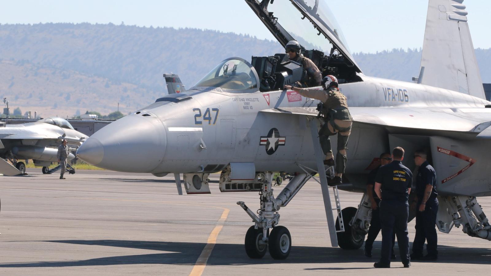 Several men working on a fighter jet on the tarmac.