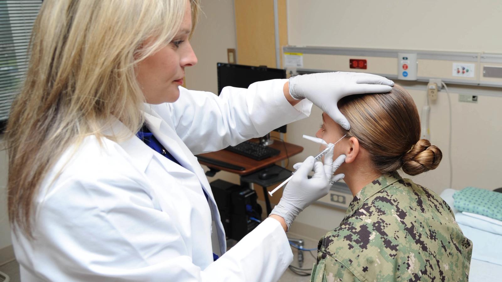 Servicewoman receives a shot administered by a doctor in her office in her head.