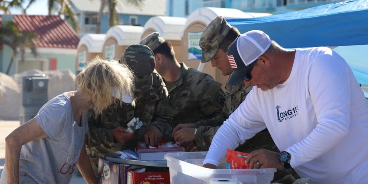Army personnel distributing supplies at a post-hurricane relief station on a beachfront.