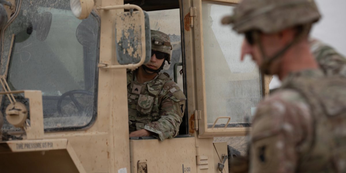 One soldier salutes another in a military vehicle.