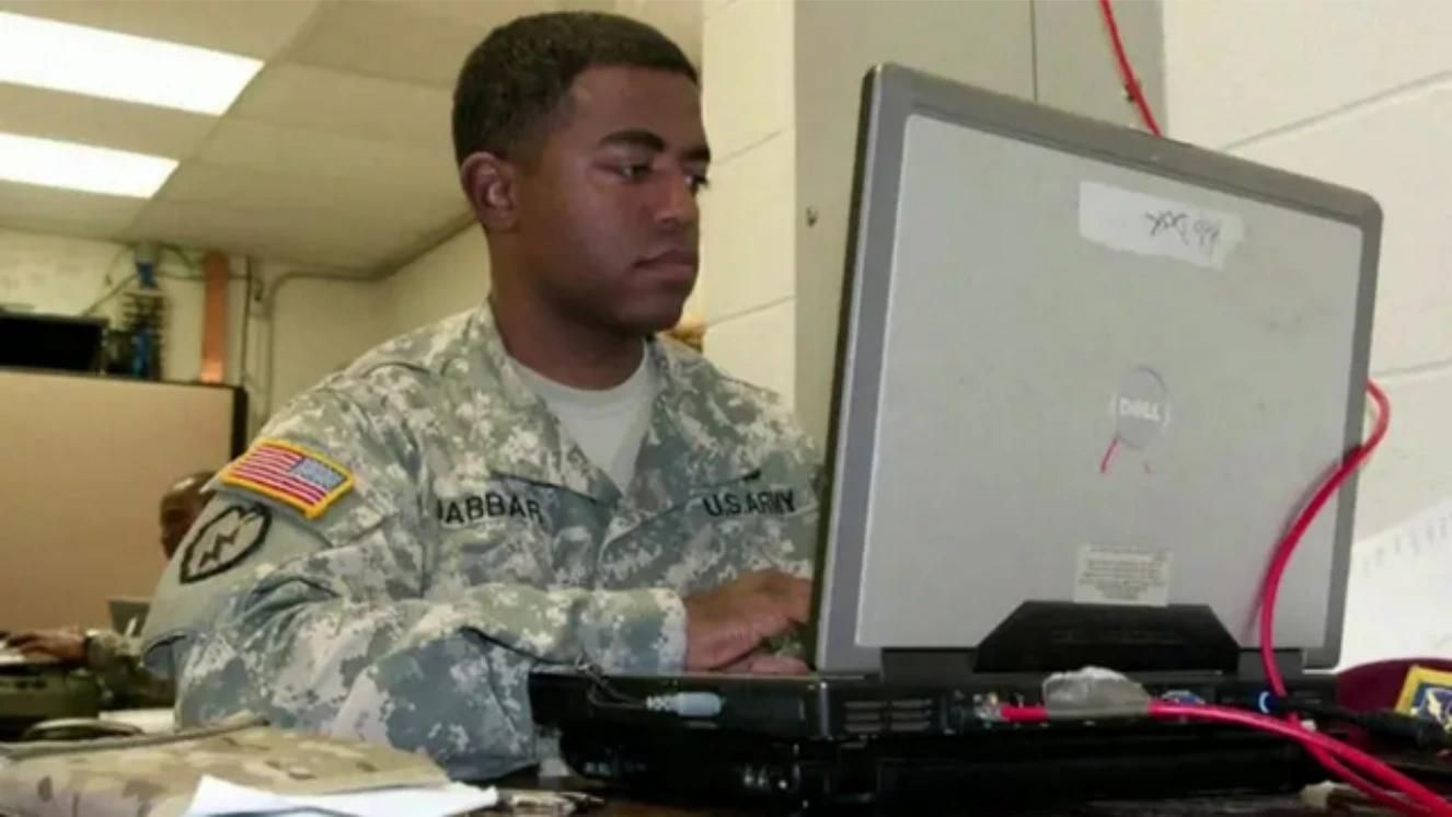 Army soldier in uniform working on a laptop in an office setting.