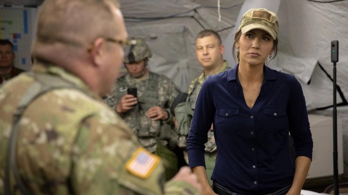Kristi Noem in military tent with Army personnel in camouflage uniforms