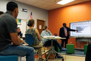 Parents of students sit in a classroom.