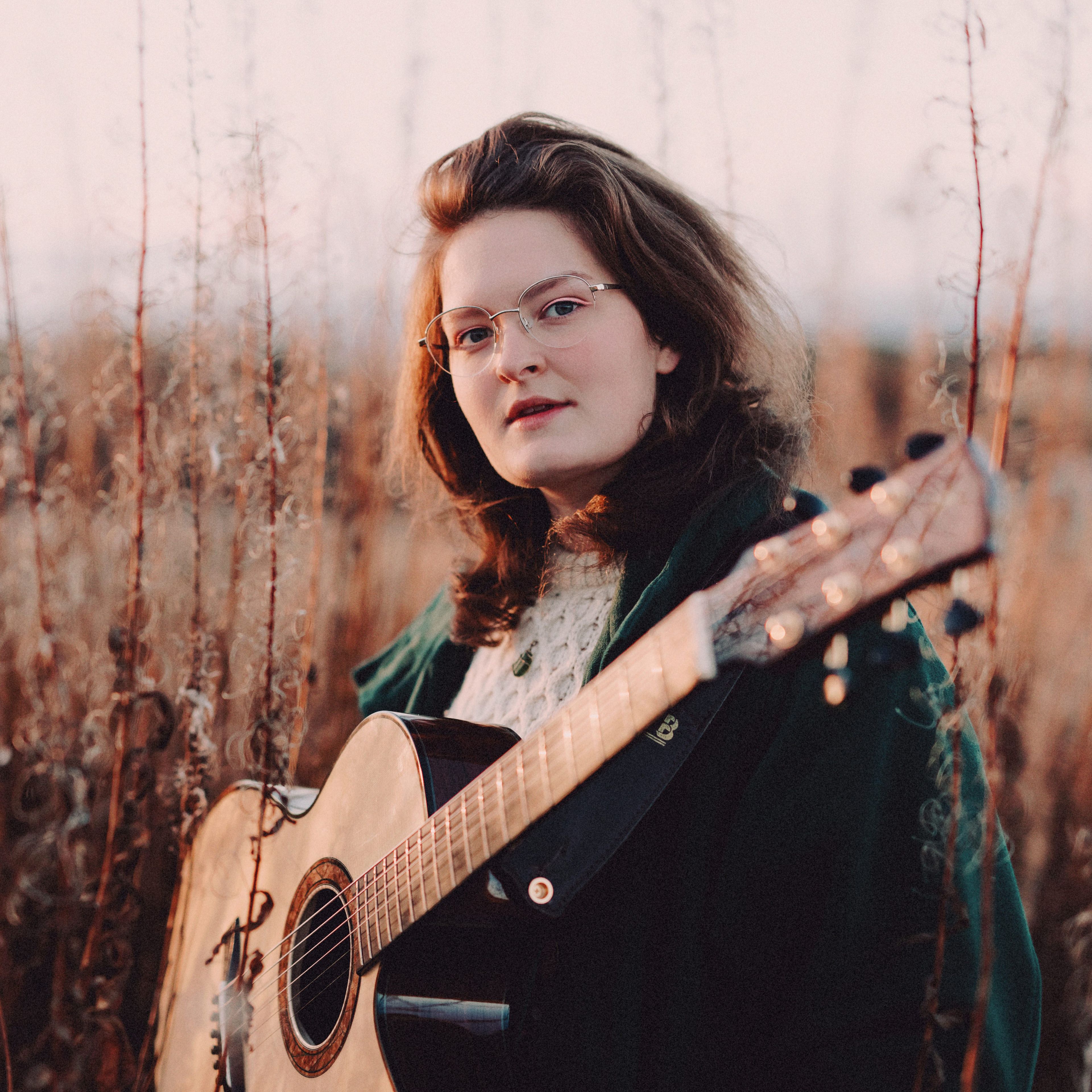 A woman stood in a field with a guitar