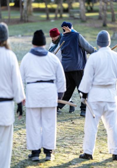 Outdoor aikido weapons training with instructor demonstrating jo technique to students in a park