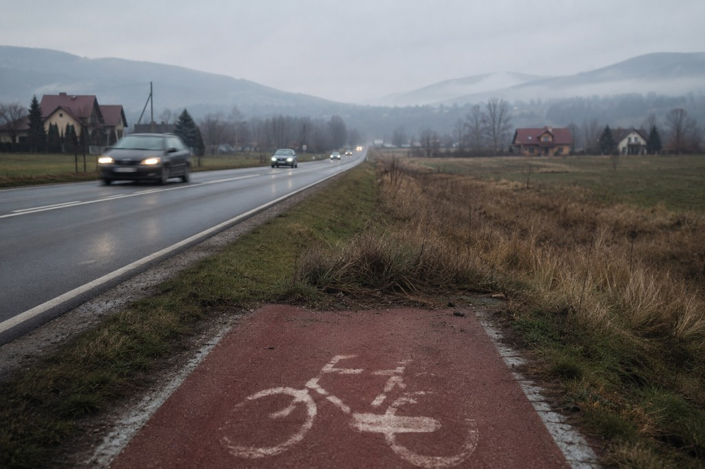 Polska droga z ruchem samochodowym; obok urwana czerwona ścieżka rowerowa z symbolem roweru, kończąca się w trawie