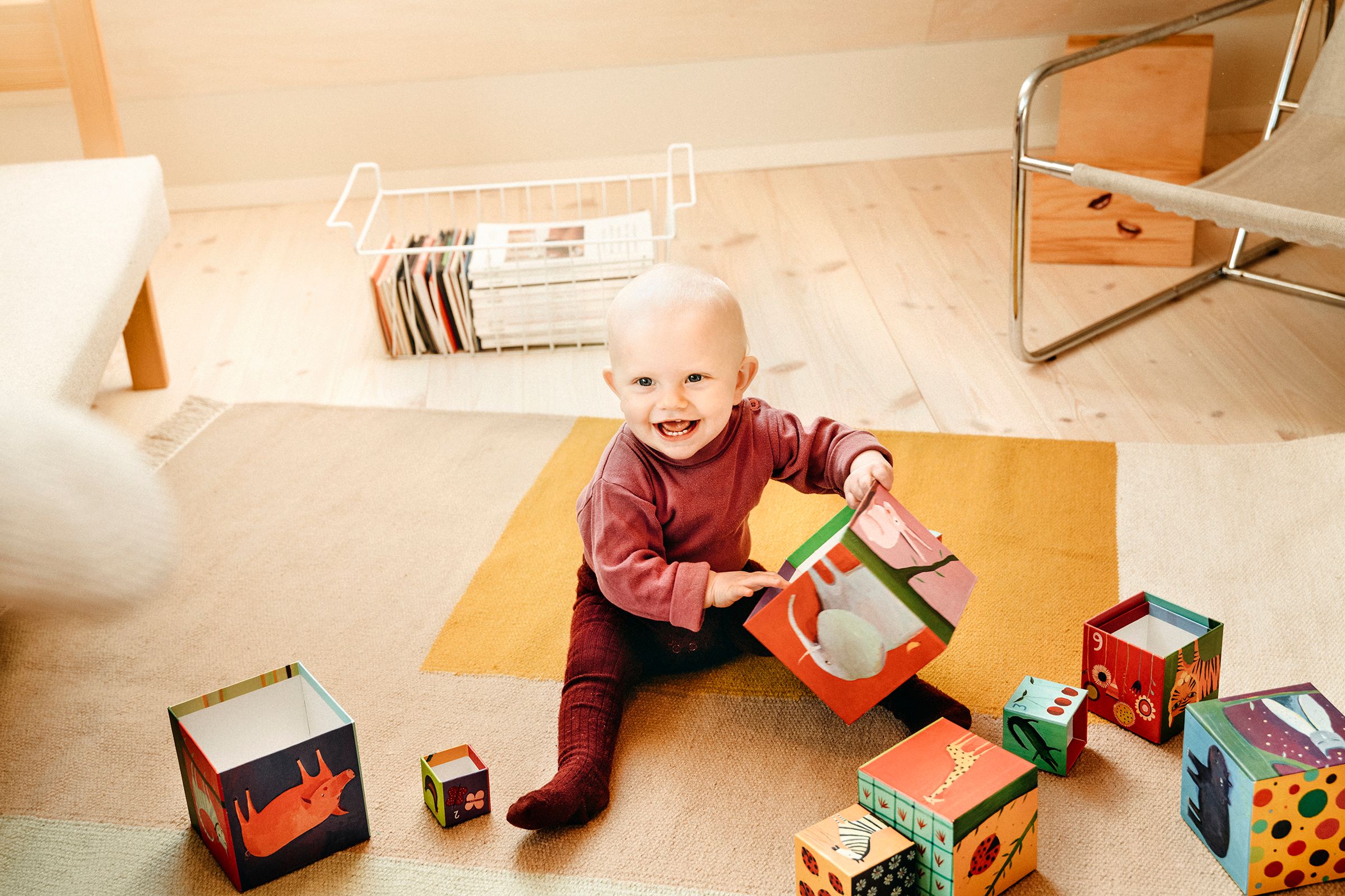 På bildet ser man en baby som sitter på gulvet med flere store treklosser den leker med. Barnet smiler glad mot kameraet.