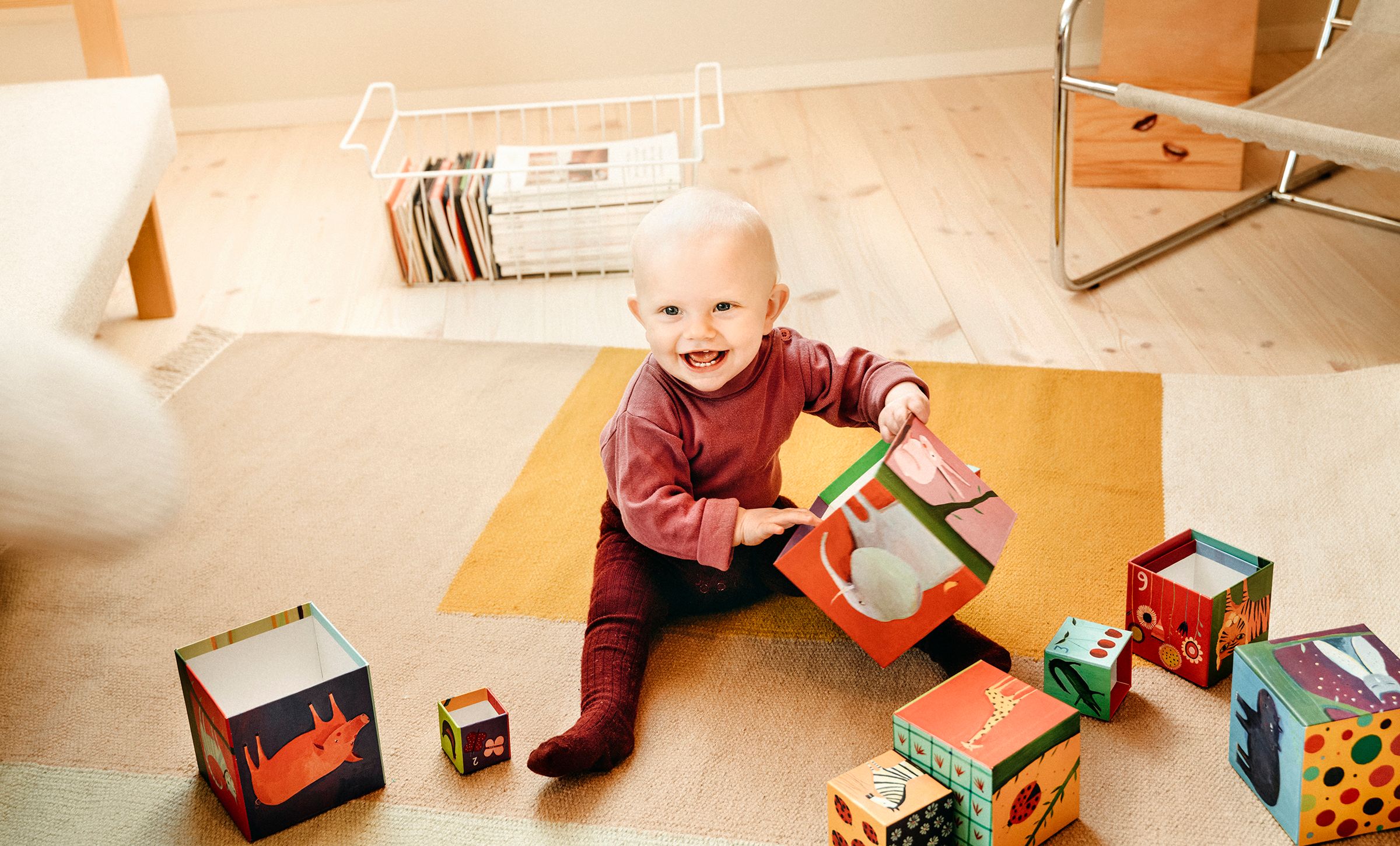 På bildet ser man en baby som sitter på gulvet med flere store treklosser den leker med. Barnet smiler glad mot kameraet.
