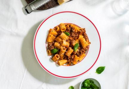 Tallerken med pasta og bolognese, på et bord med hvit klede.