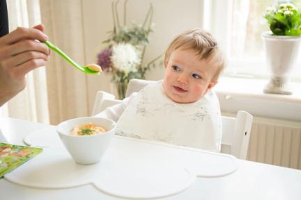 Bebis vid matbord som ser skeptiskt på matsked