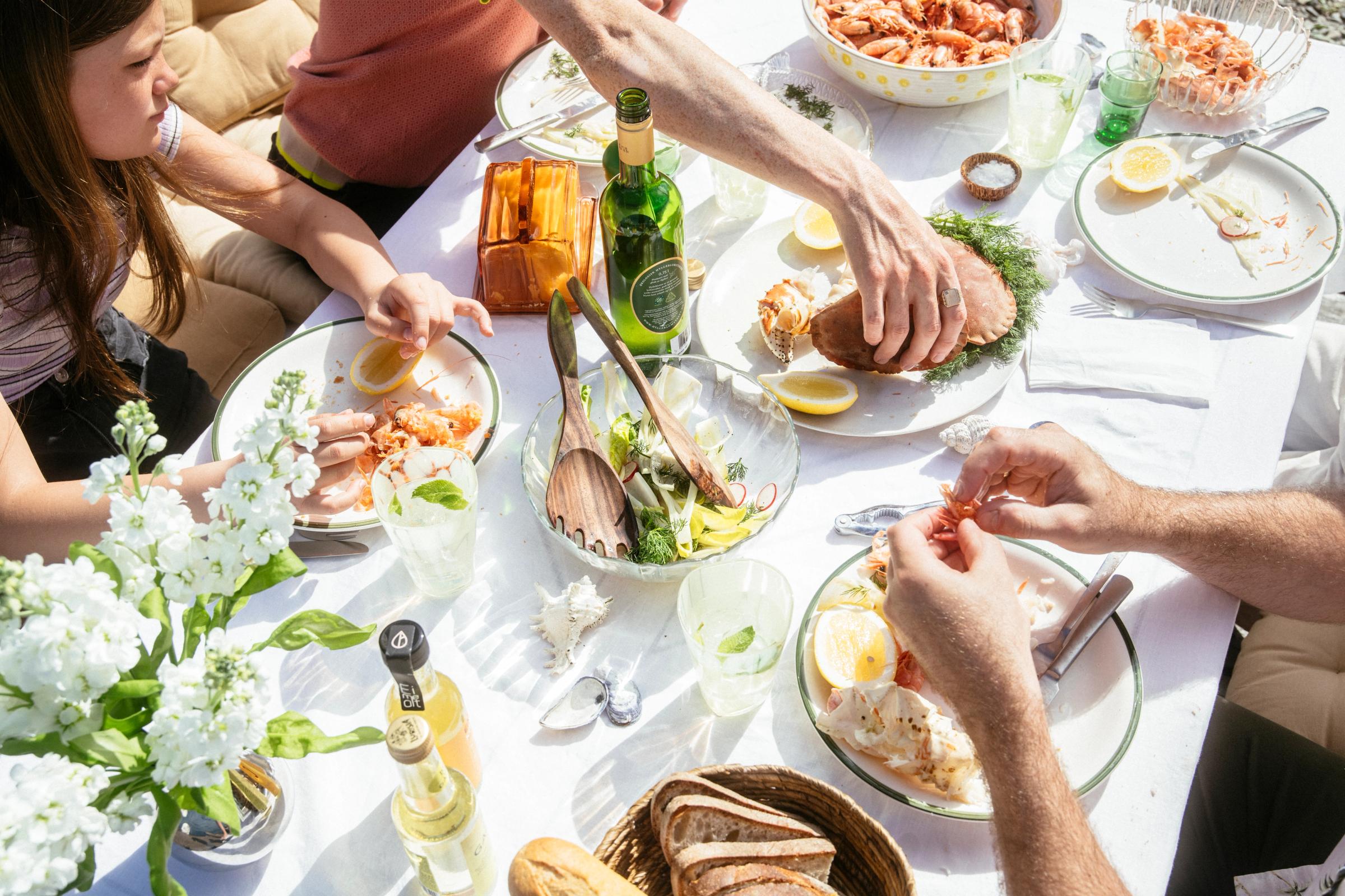 Bildet inneholder en familie som sitter ved bordet og spiser sommermat og reker