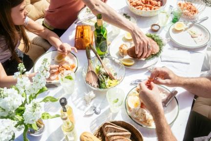 Bildet inneholder en familie som sitter ved bordet og spiser sommermat og reker