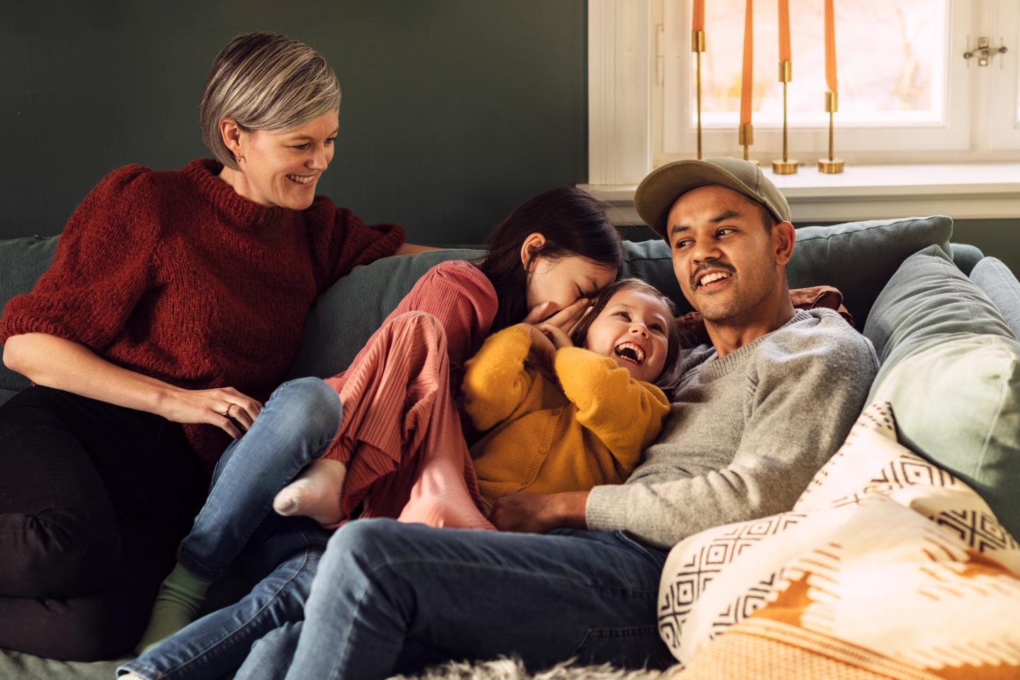 Eine Familie mit zwei Töchtern sitzt auf dem Sofa in der Abendsonne und alle lachen.