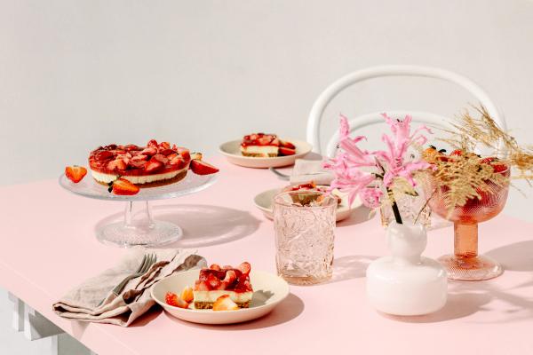 På bildet ser man et bord med rosa duk. På bordet står et kakefat med det som ser ut til å være en ostekake.