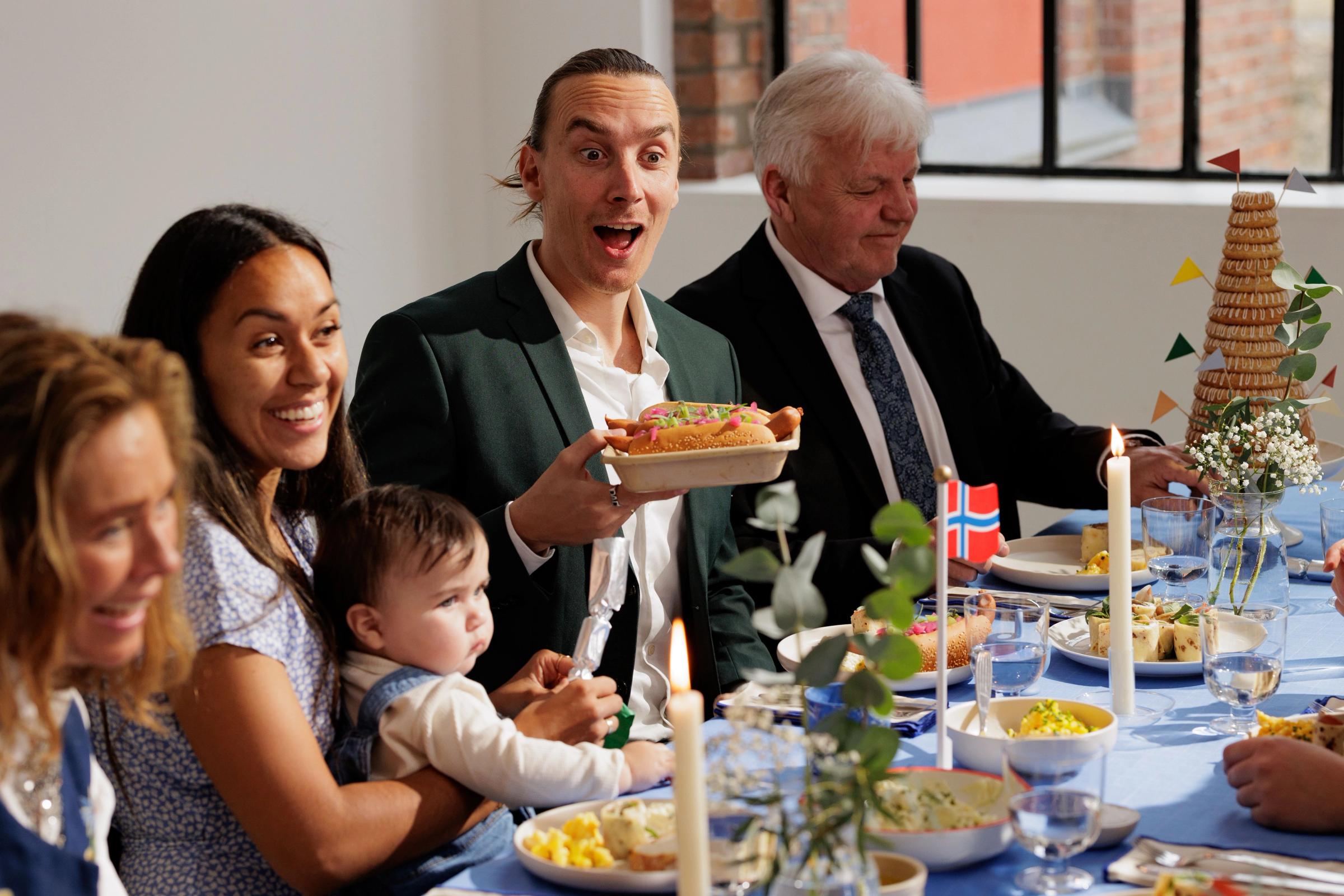 Bildet inneholder en familie som sitter ved bordet og spiser mat på 17. mai.