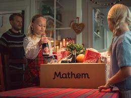 Bilden visar en två barn som packar upp varor från en Mathemlåda, i bakgrunden syns deras pappa. Bilden ger julkänslor.