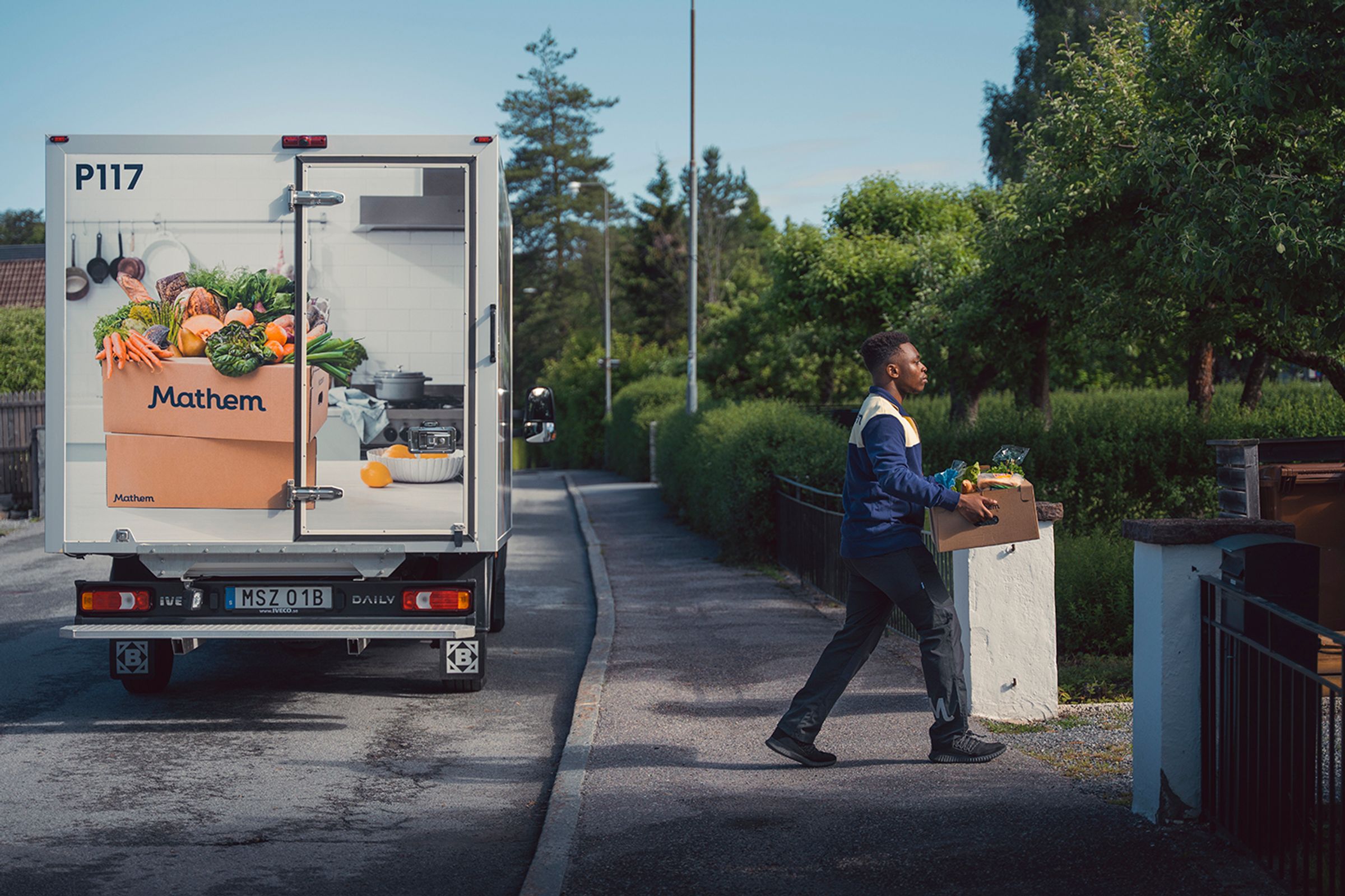 På bilden syns en person bära en Mathem-låda. I bakgrunden syns en Mathem-van.