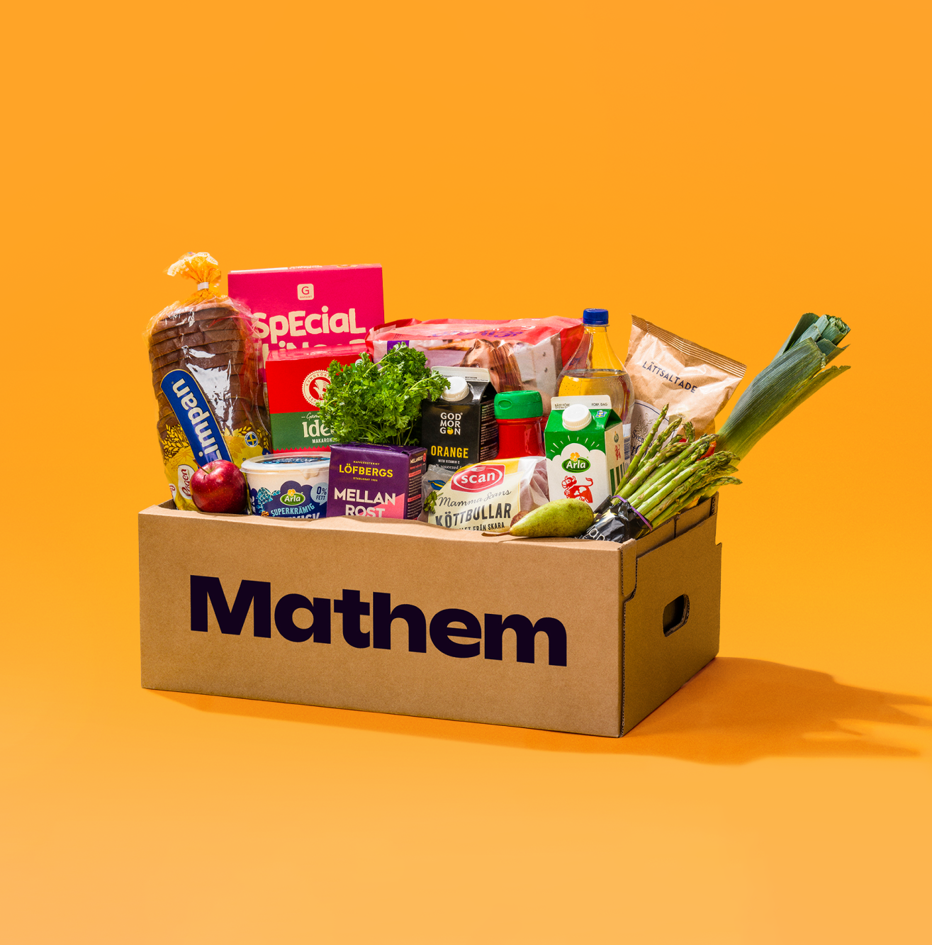 På bilden syns en Mathemlåda fylld med varor mot en orange bakgrund