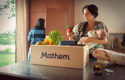 Kvinna håller i bebis och plockar upp en klämmatspåse ur Mathemlåda