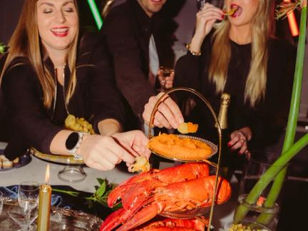 På bilden syns flera personer äta mat från en hög bricka med skaldjur och löjrom.