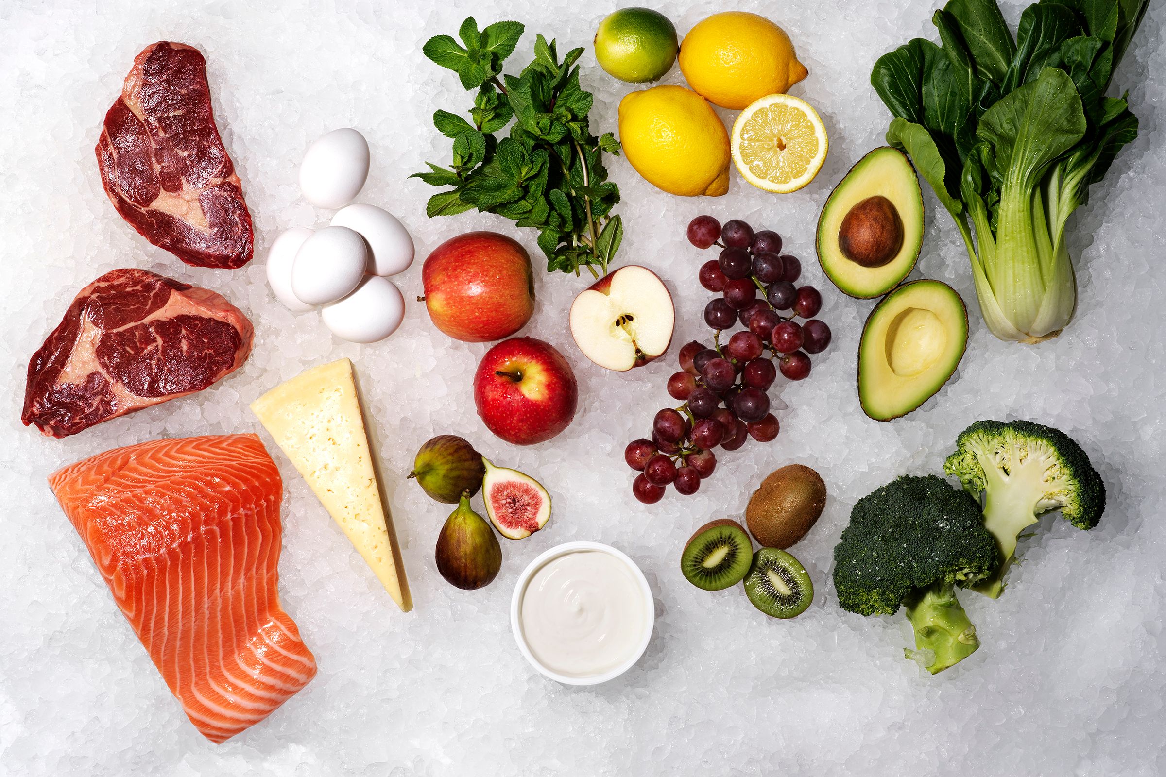 På bilden syns frukt, grönsaker, kött och fisk på en ljus marmorskiva