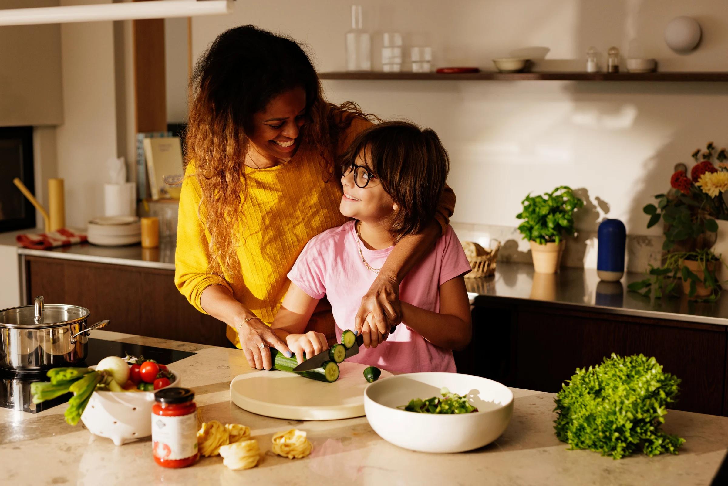 Mamma og datter på kjøkkenet som lager mat/kutter agurk/grønnsaker