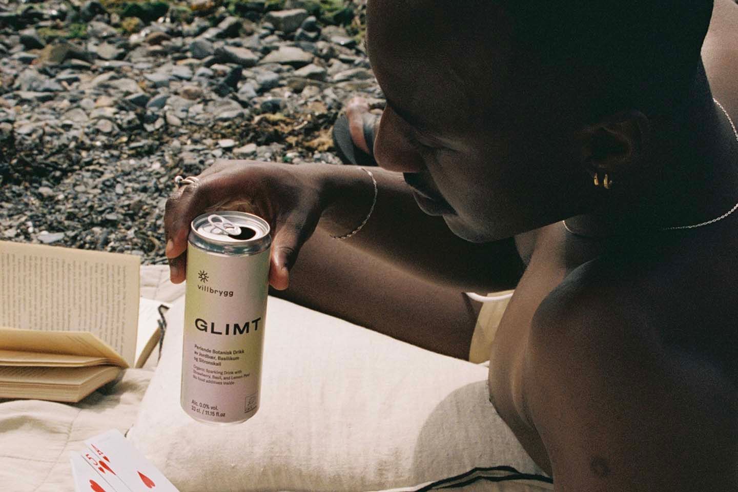 På bildet ser man en mann ligge på et strandpledd og drikke av en boks fra Villbrygg.