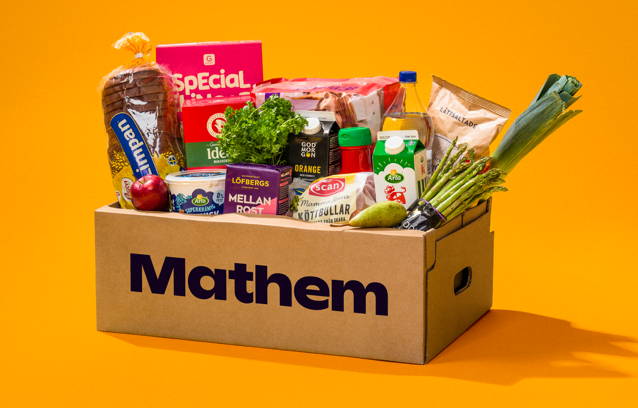 På bilden syns en Mathemlåda fylld med varor mot en orange bakgrund