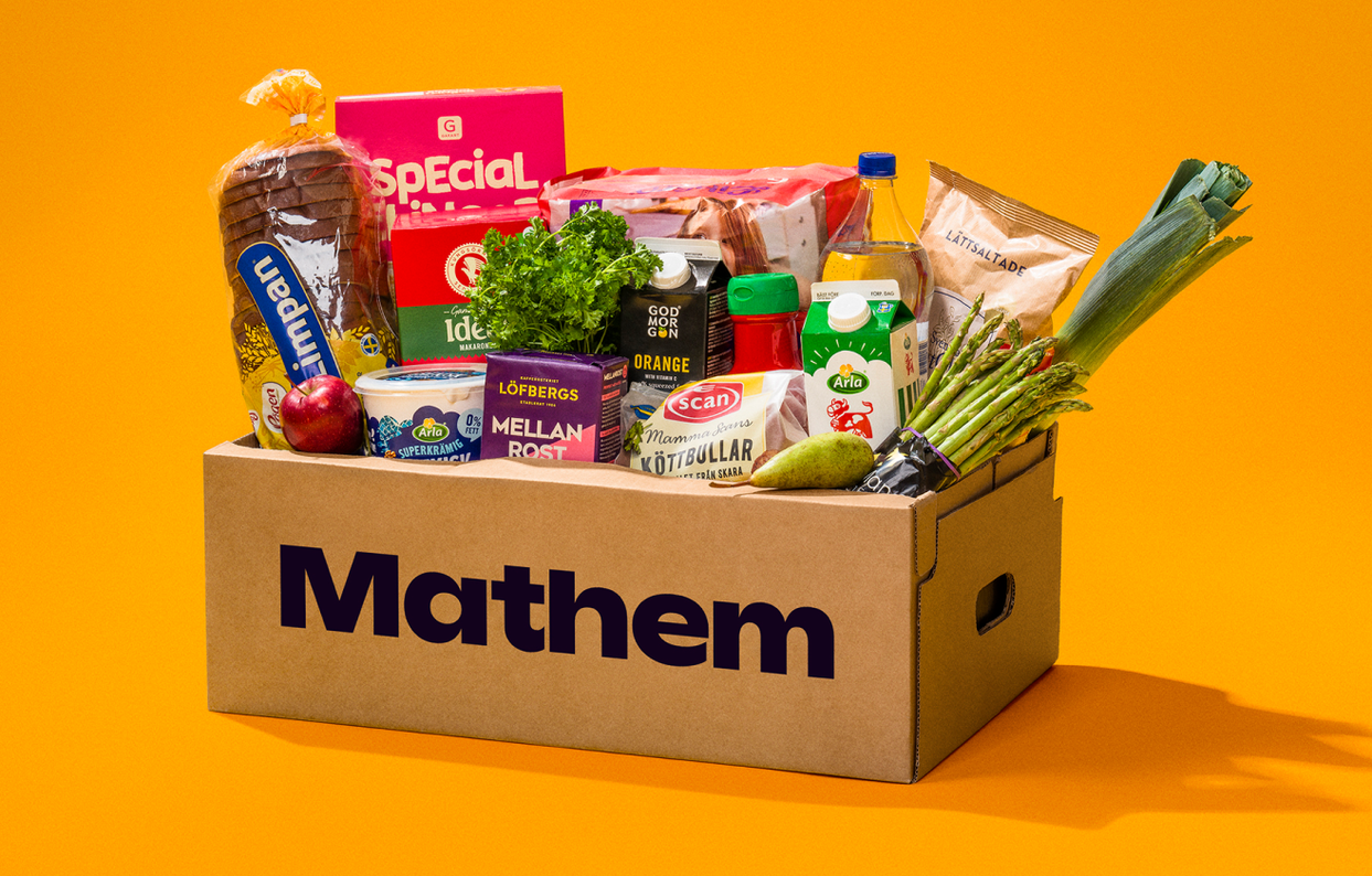 På bilden syns en Mathemlåda fylld med varor mot en orange bakgrund