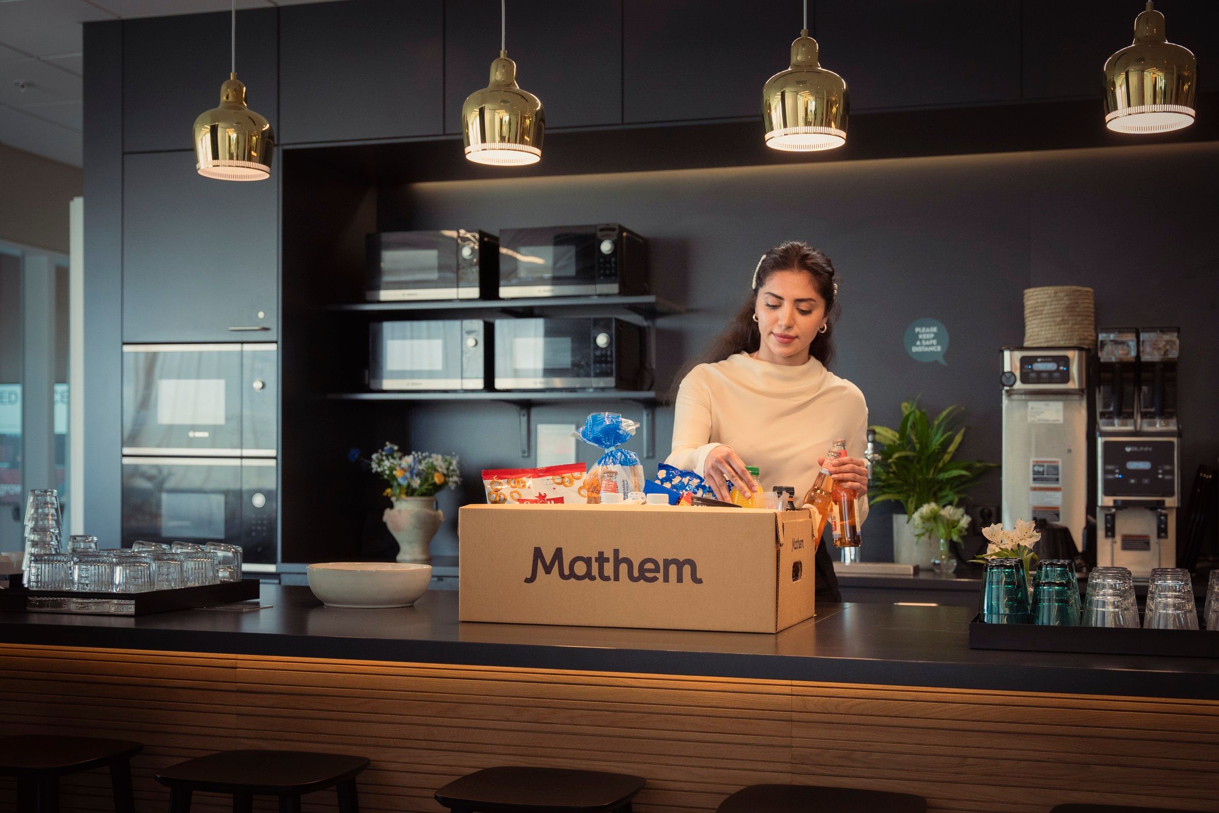 Person packar upp varor från en Mathemlåda, i ett kontorskök