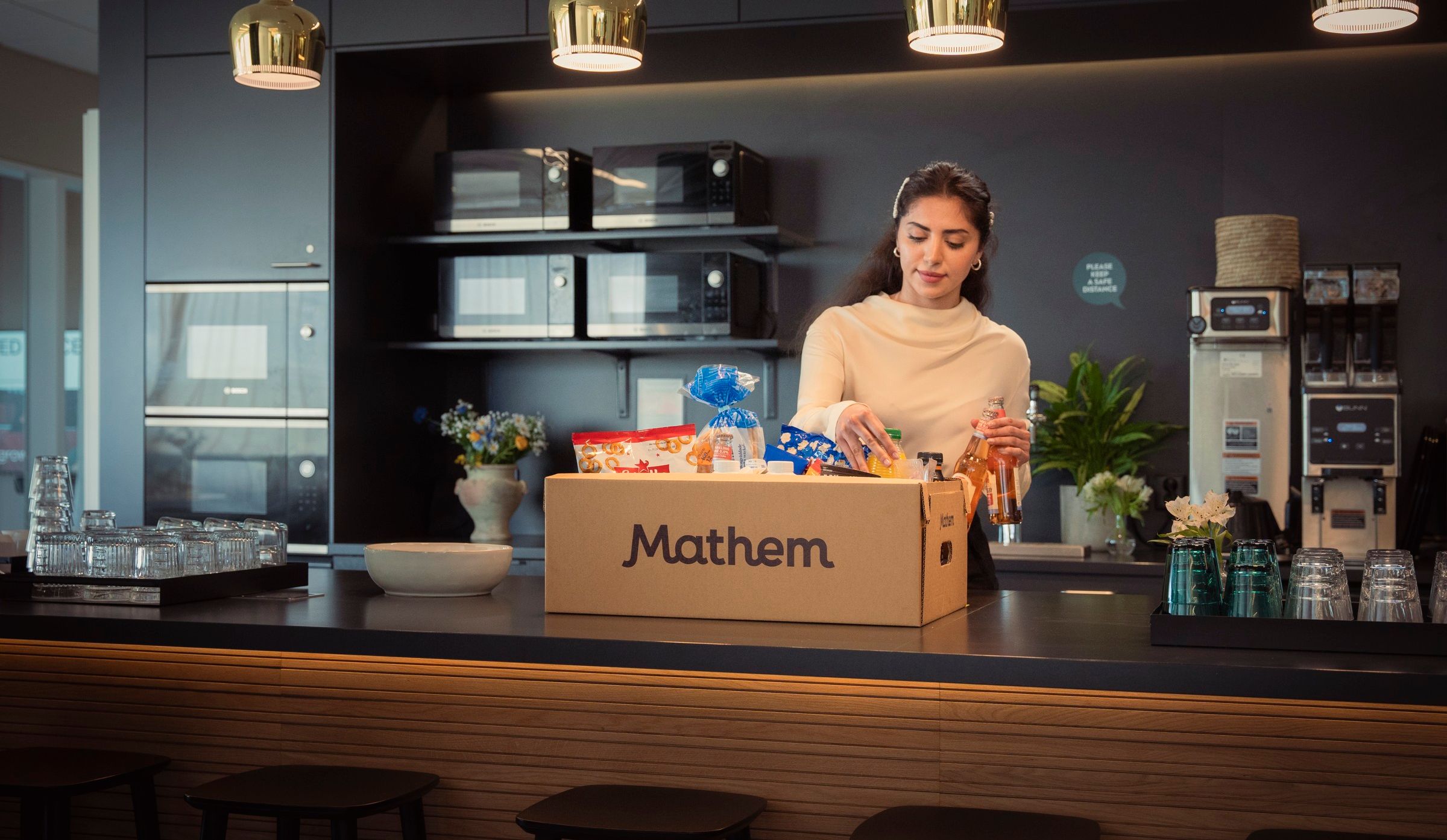 Person packar upp varor från en Mathemlåda, i ett kontorskök