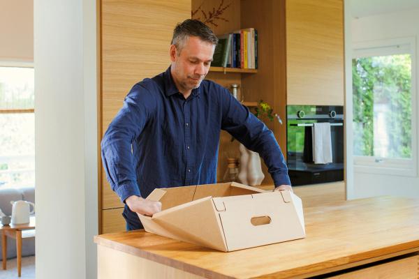 På bildet ser man en person som gjør steg 1: Dytter langsidene utover slik av esken blir helt flat.