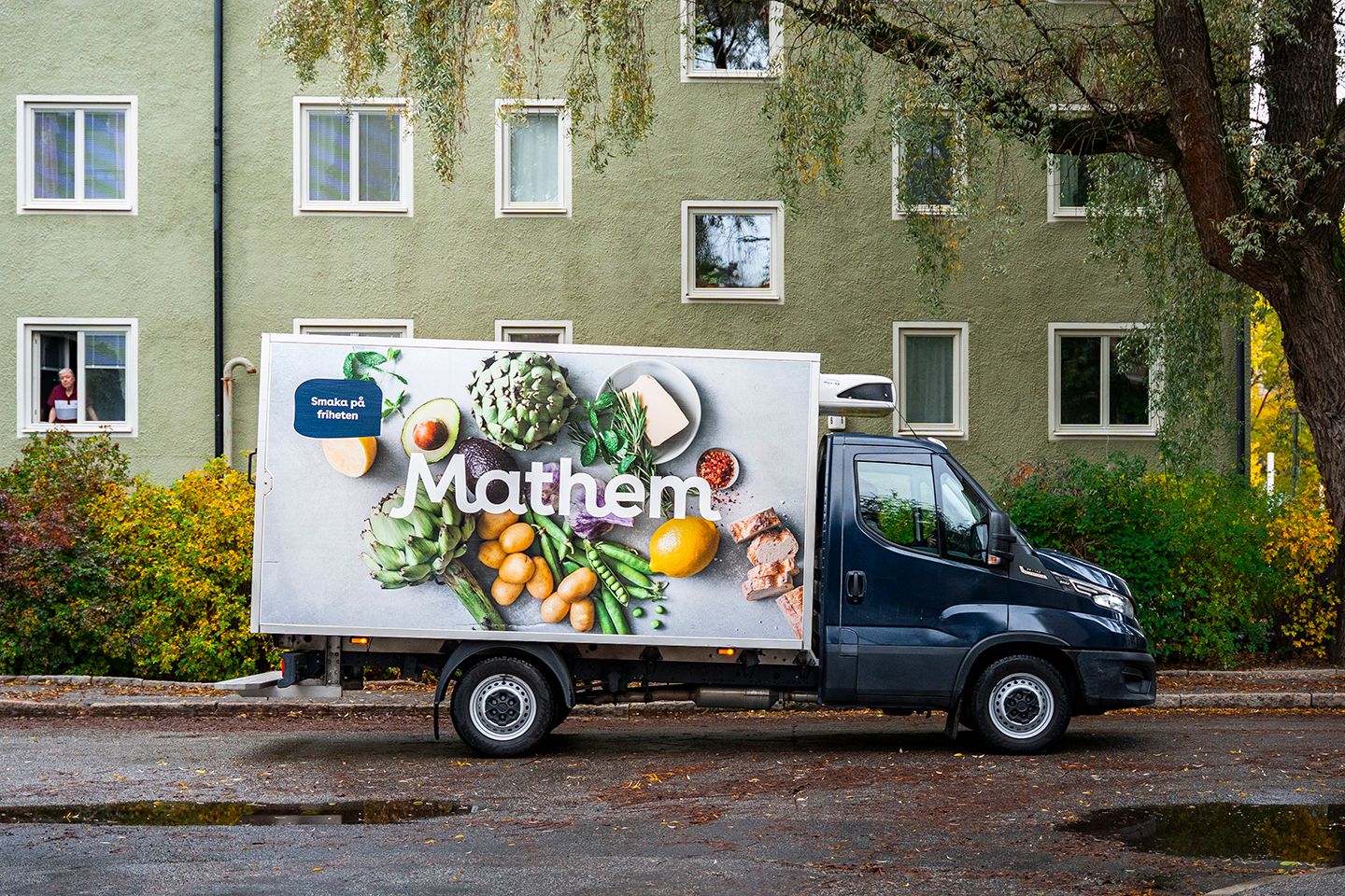Mathembil står utanför ett grönt hyreshus. 