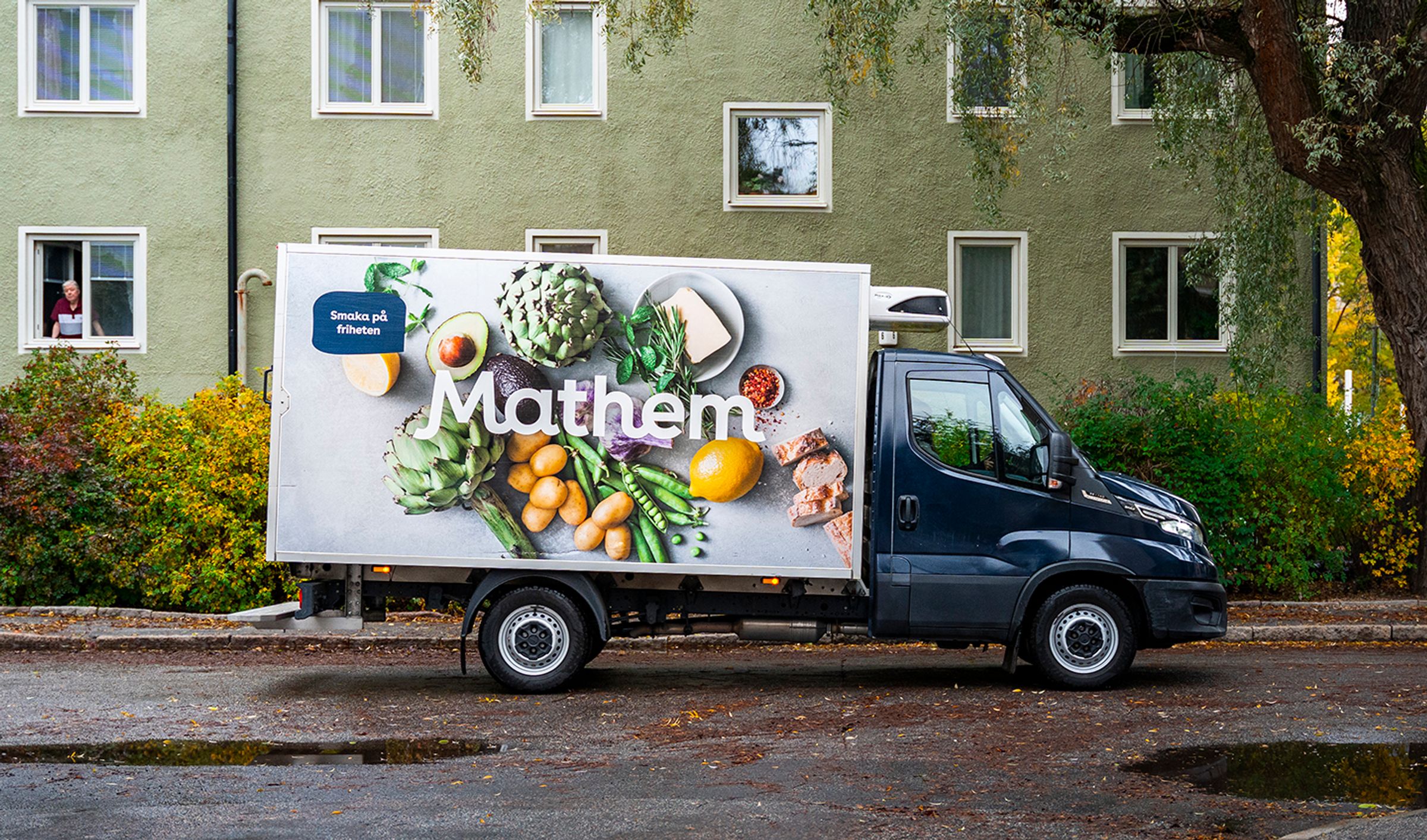 Mathembil står utanför ett grönt hyreshus.