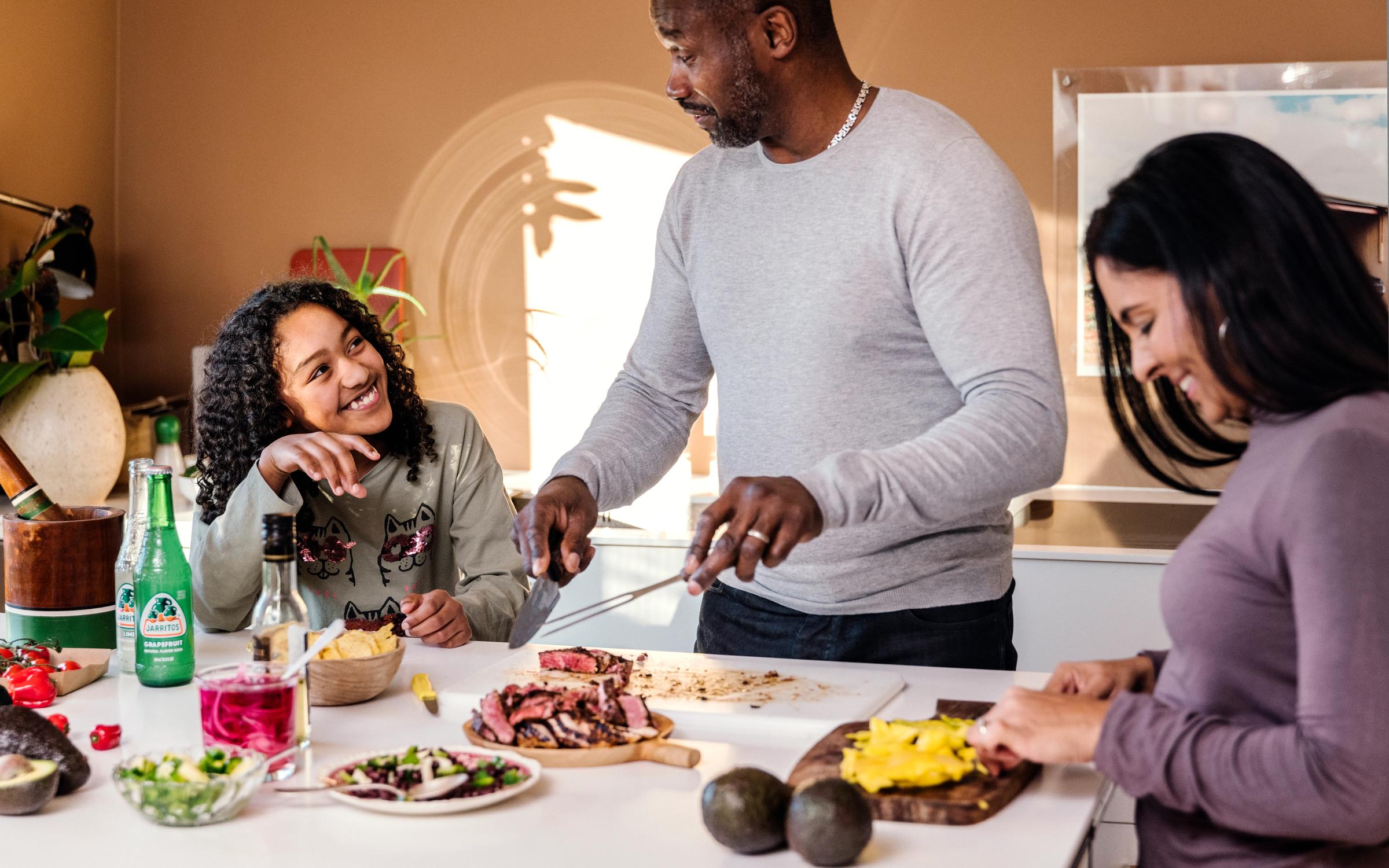 Bildet inneholder en familie som står på kjøkken og lager mat