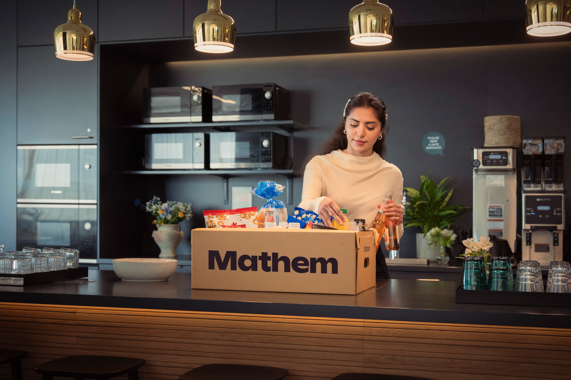 Person packar upp varor från en Mathemlåda, i ett kontorskök