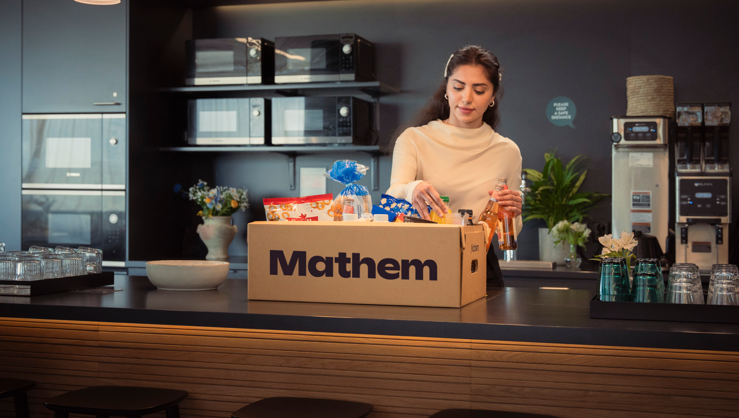 Person packar upp varor från en Mathemlåda, i ett kontorskök