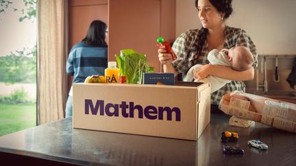 Kvinna håller i bebis och plockar upp en klämmatspåse ur Mathemlåda