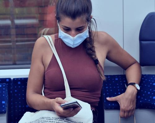 woman on public transportation with a mobile phone wearing a mask