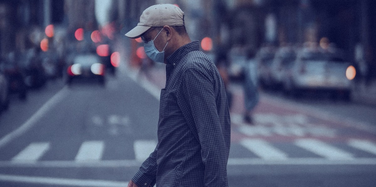 Man walking across a city street wearing a mask