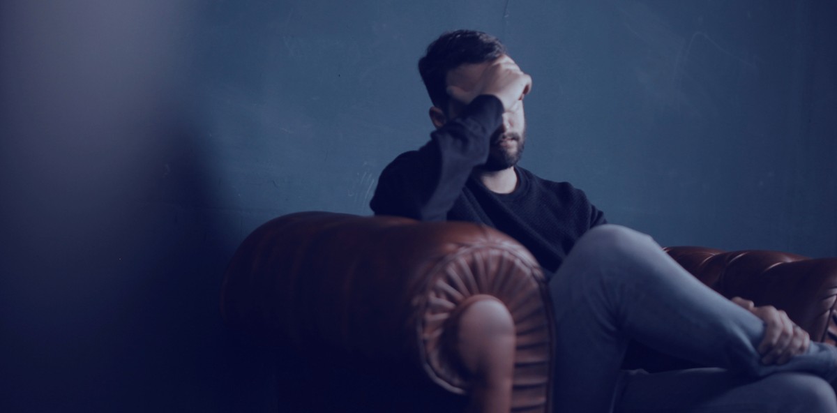 Man on couch with one hand on his forehead